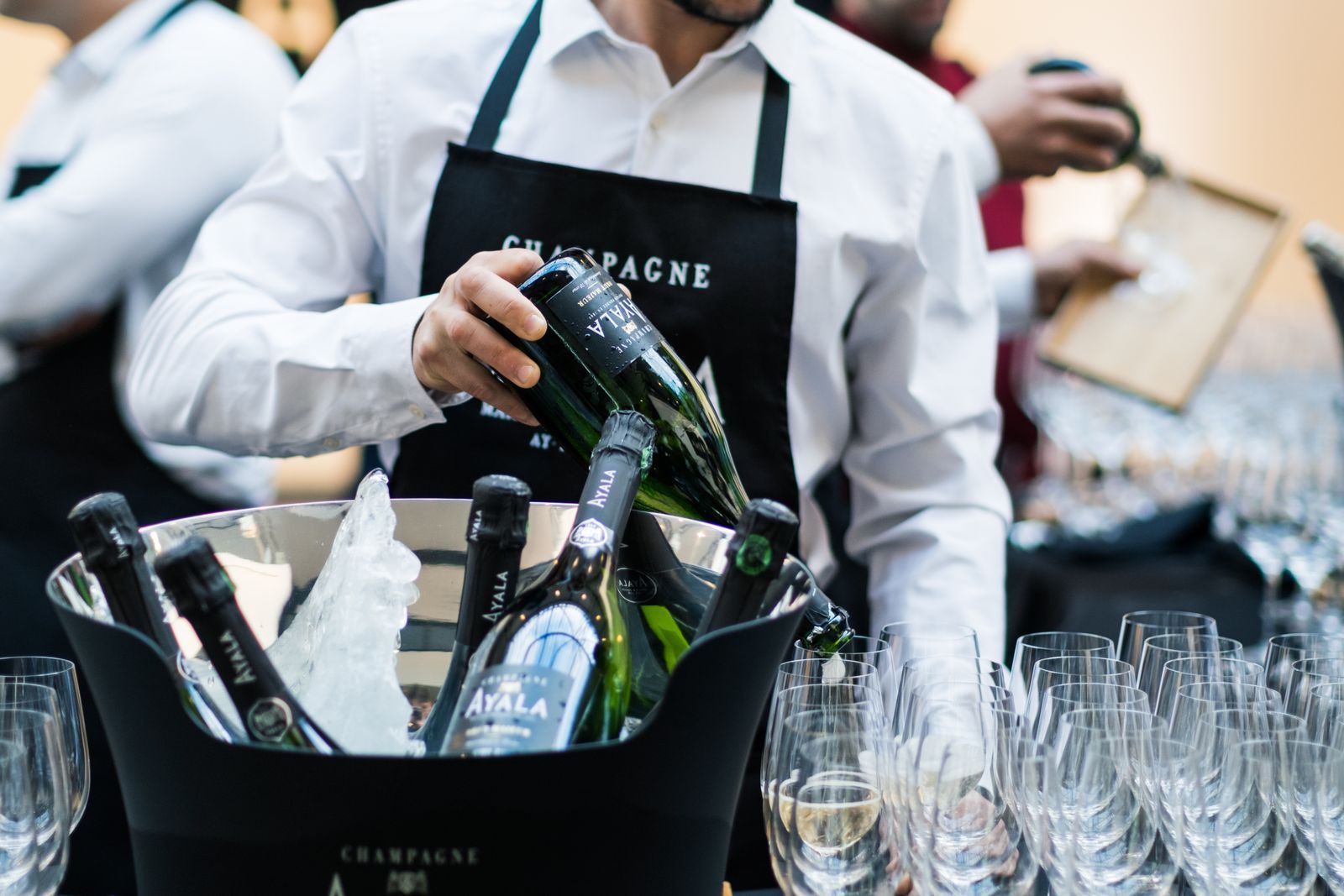 Uniformed server pouring champagne beside an ice bucket, the kind of attentive service found on river cruises with butler service