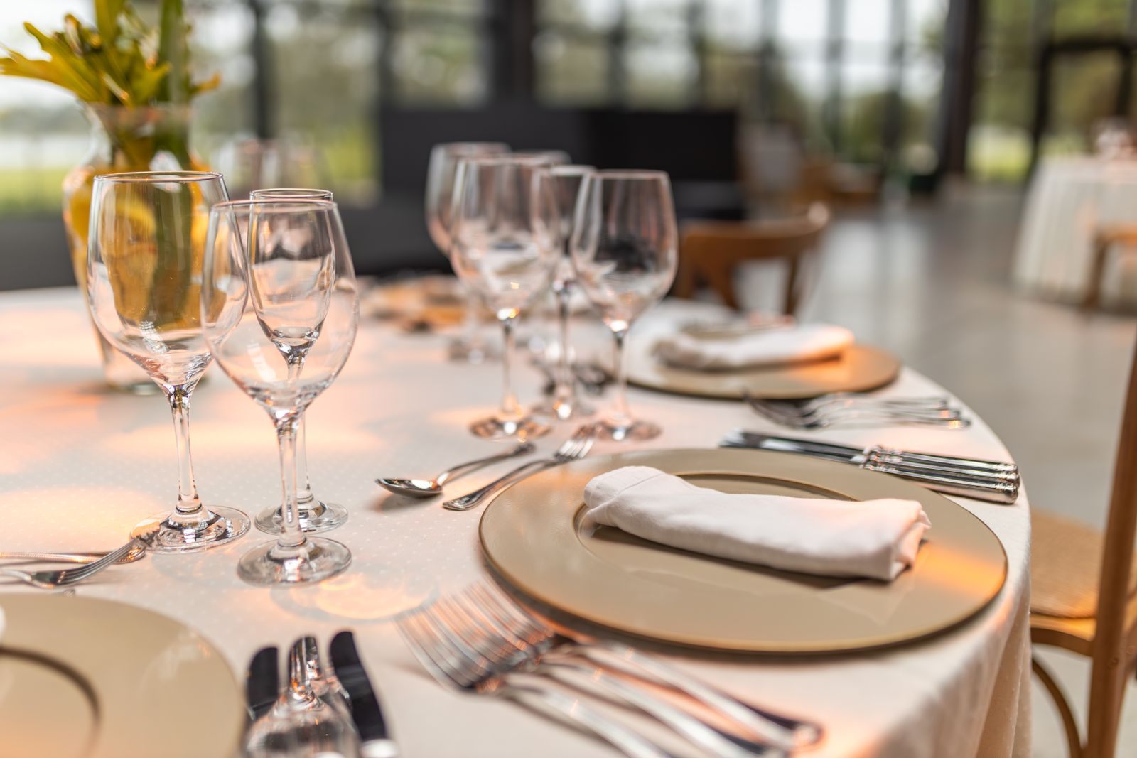 Fine-dining table set with crystal glasses, gold chargers and folded napkins beside large windows