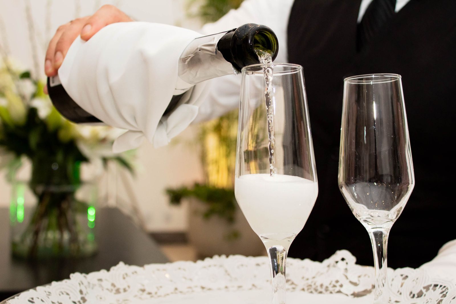Champagne poured into flutes by a server with a white napkin