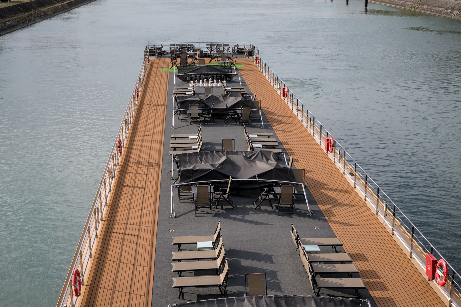 Long teak sun deck with loungers and shaded tables on top of a river cruise ship, a feature of the most luxurious river cruise ships